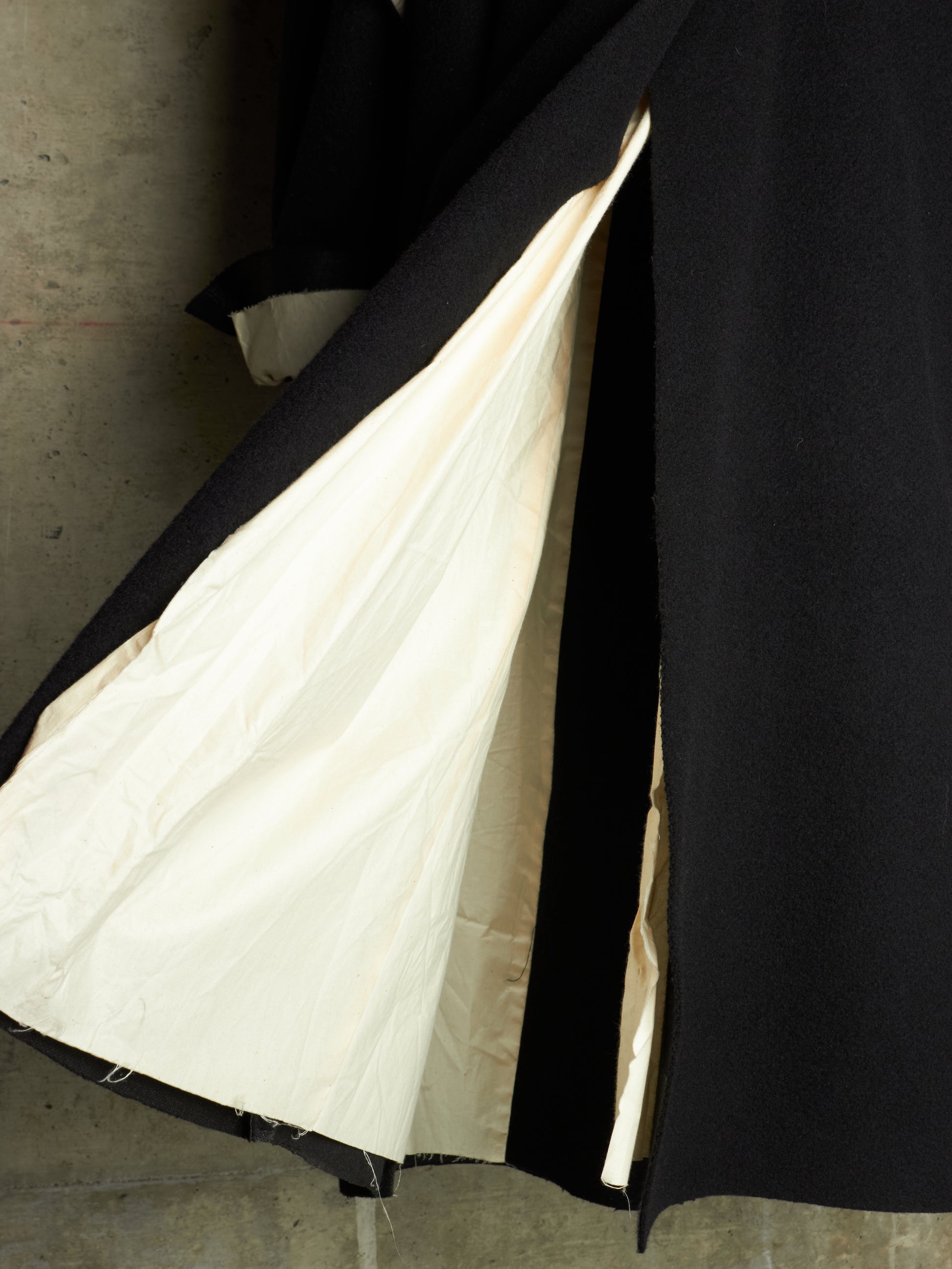 A close-up of a black coat or garment with a large cream-colored lining pulled open, showing the interior against a dark background.
