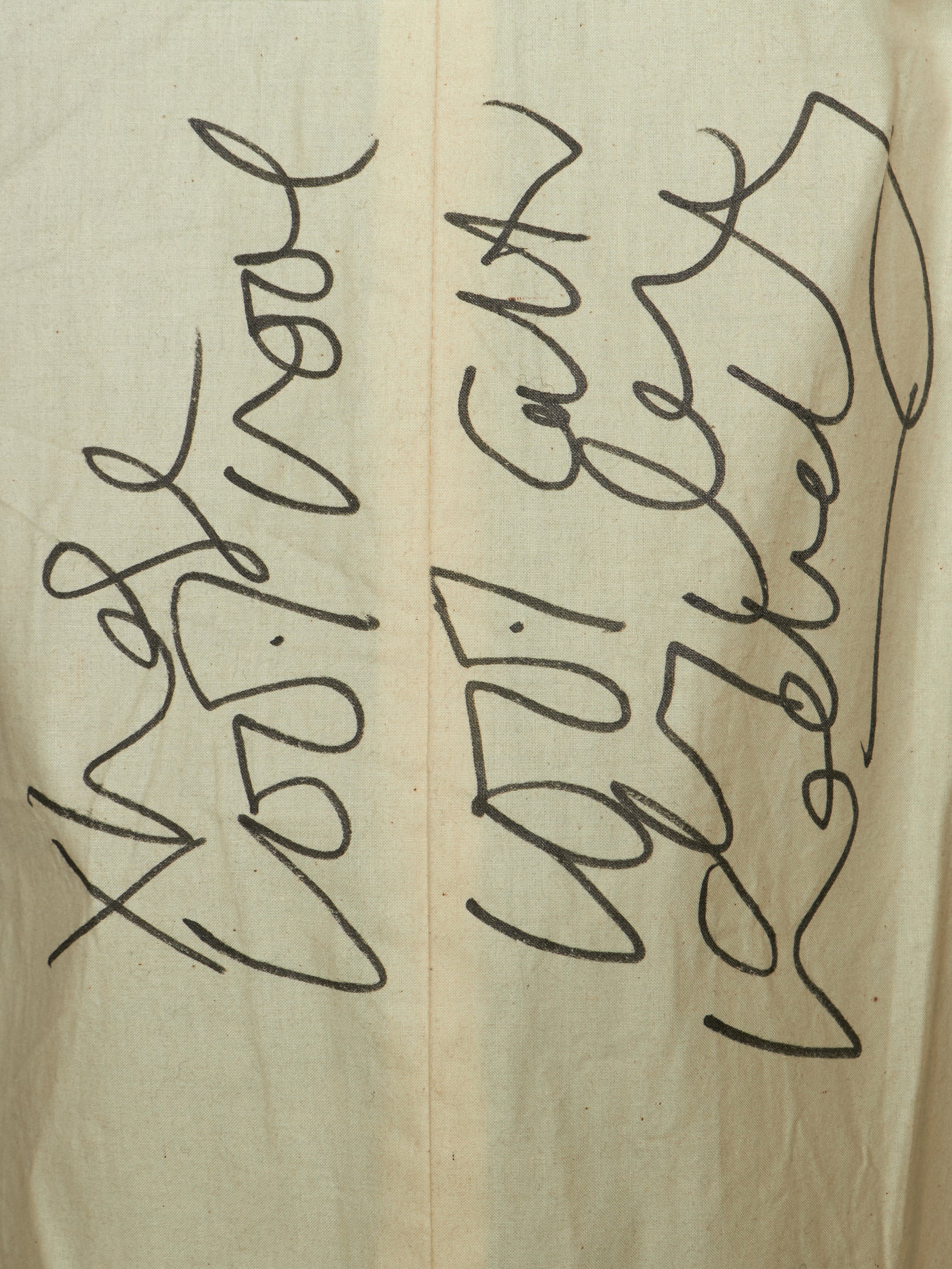 A close-up of a beige fabric surface with black handwritten or printed abstract script running vertically across it.