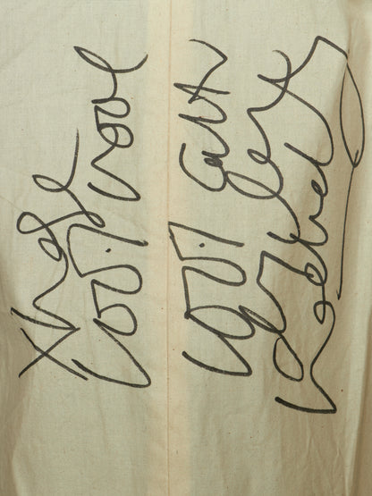 A close-up of a beige fabric surface with black handwritten or printed abstract script running vertically across it.
