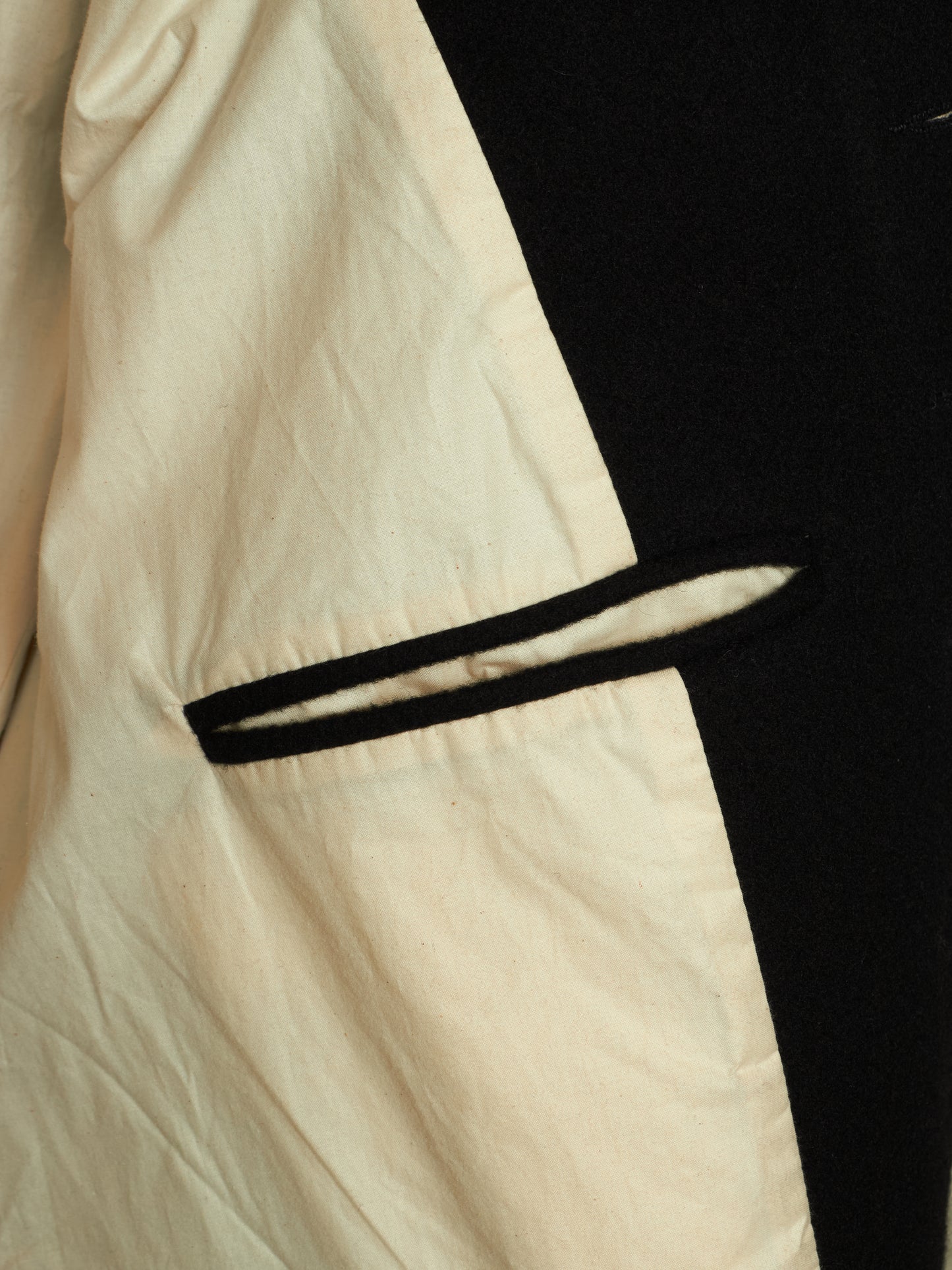 Close-up of a garment showing a cream-colored fabric body with a black trim detail and a black side panel.