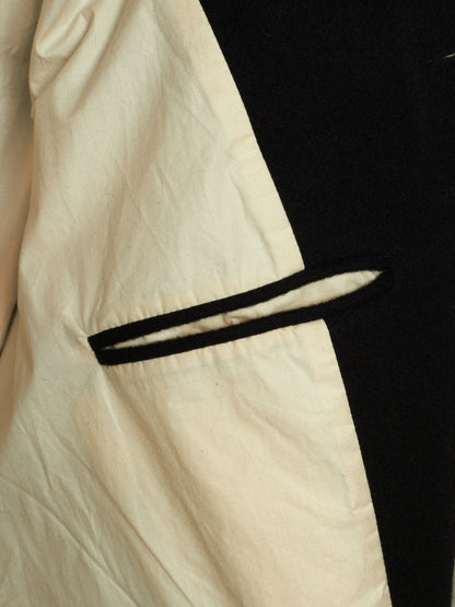 Close-up of a garment showing a cream-colored fabric body with a black trim detail and a black side panel.