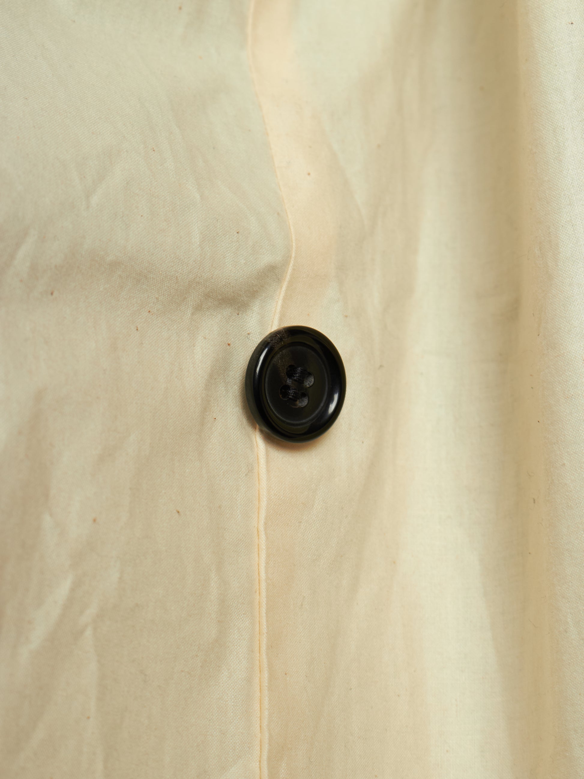 Close-up of a cream-colored fabric garment with a single black button on the front.