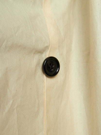 Close-up of a cream-colored fabric garment with a single black button on the front.