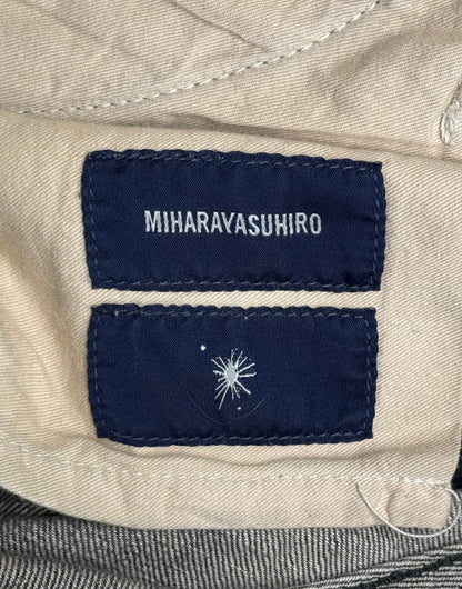A close-up shows the Mihara Yasuhiro AW10 Double-pockets Repair Patchwork Selvedge Denim label sewn onto beige fabric above a navy tag with a white abstract design.