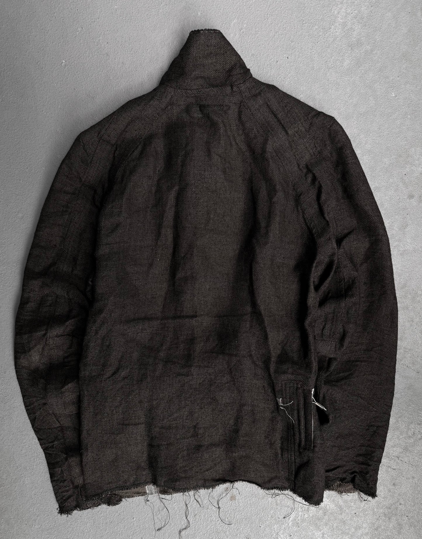 The TaichiMurakami “Coin” Taped Seam Collarless Work Blazer, shown back view on a light gray surface, features frayed edges, a wrinkled textured fabric, and industrial minimalism-inspired details for an unfinished look.