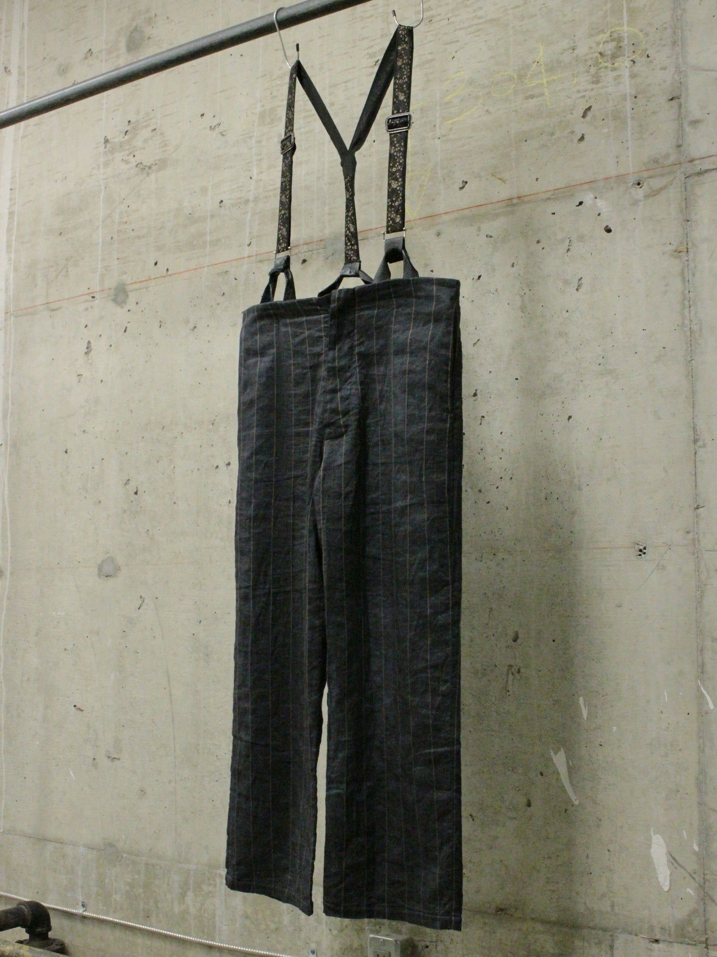 Dark denim overalls hanging on a metal rod against a concrete wall.