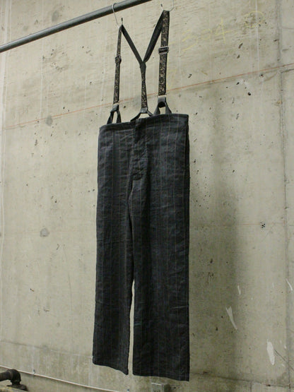 Dark denim overalls hanging on a metal rod against a concrete wall.
