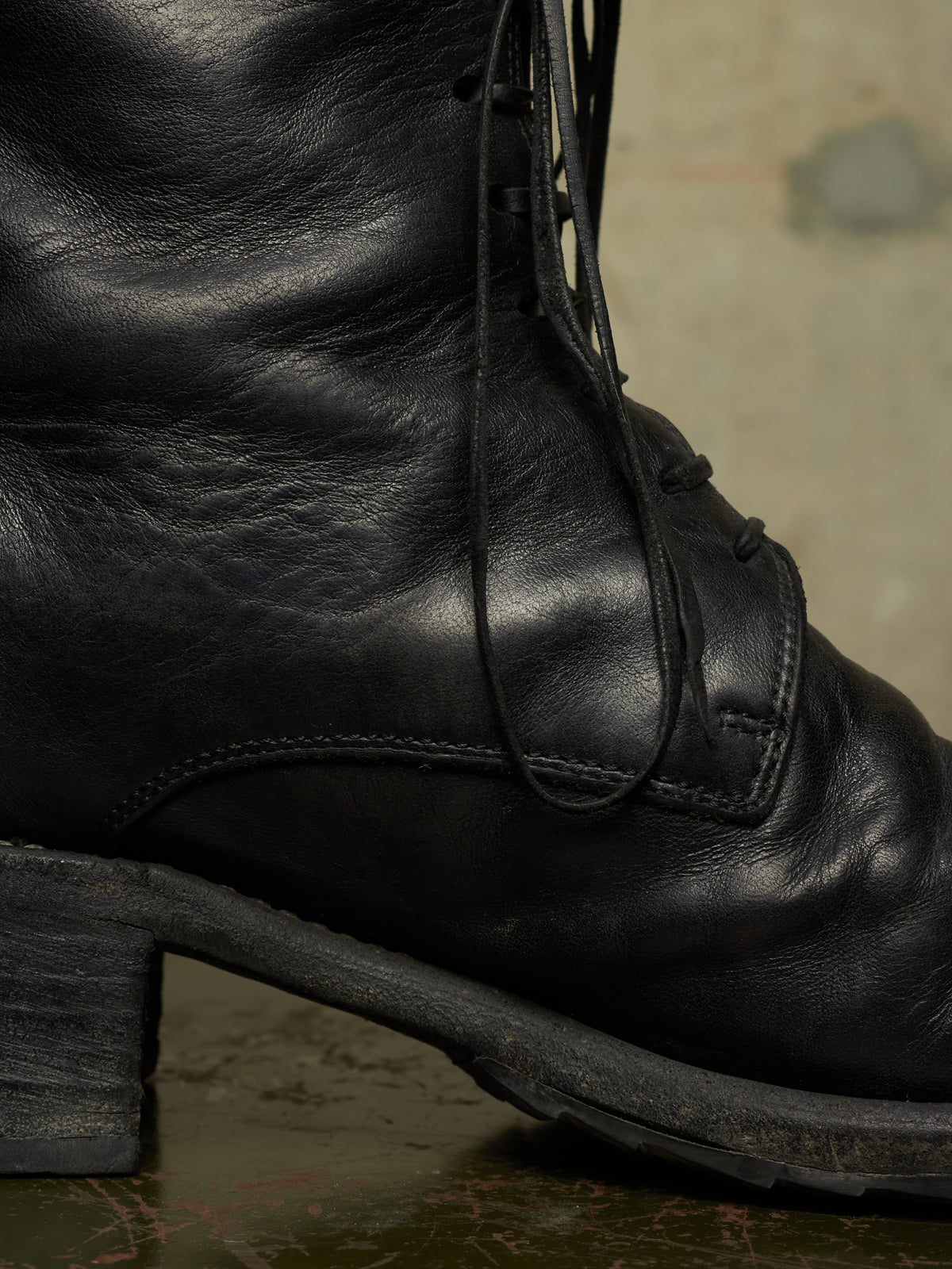Close-up of a black leather lace-up boot with a chunky block heel, showing the side profile and textured leather surface.