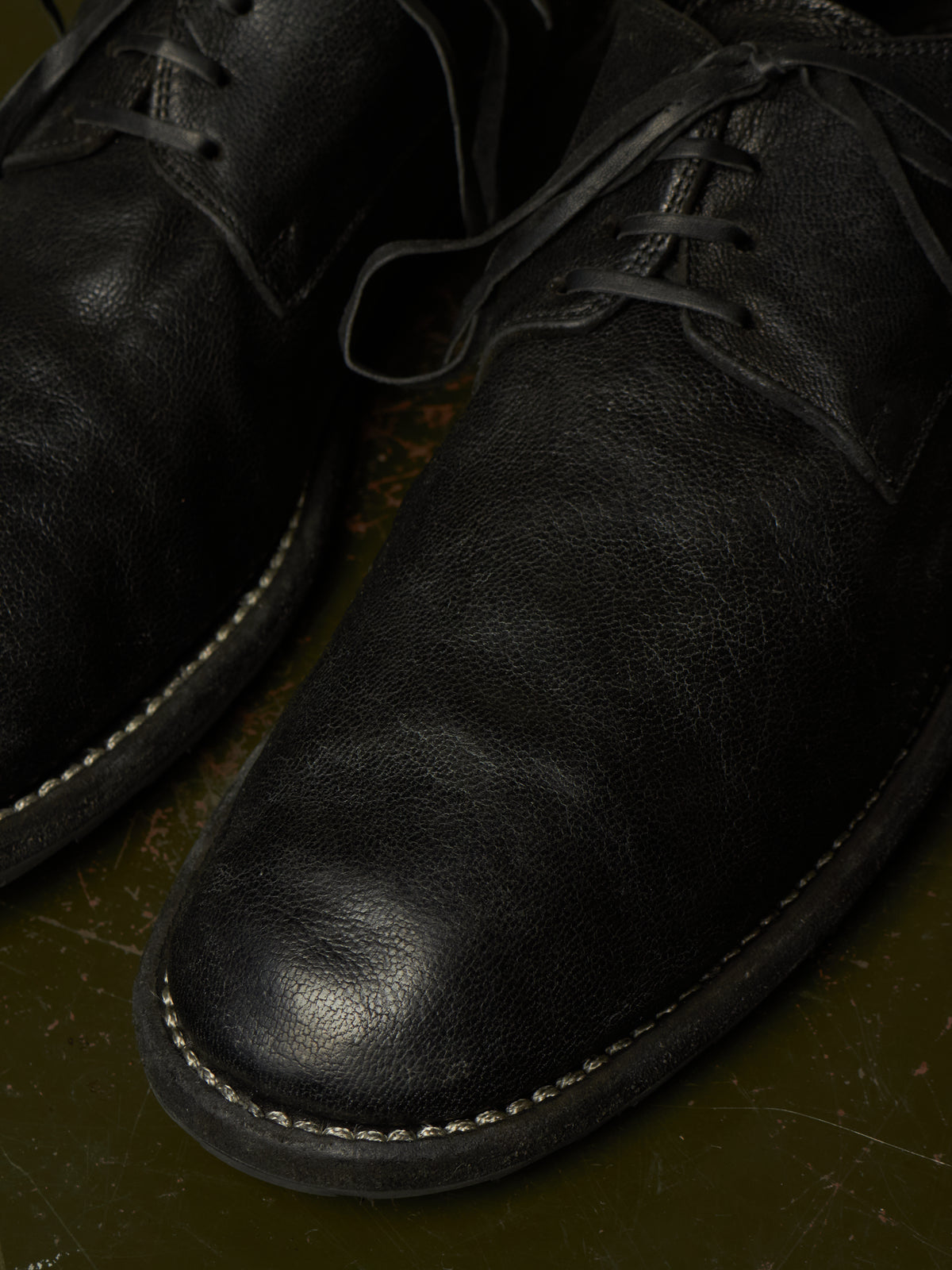 Close-up of a pair of black leather lace-up shoes resting on a dark olive green textured surface.