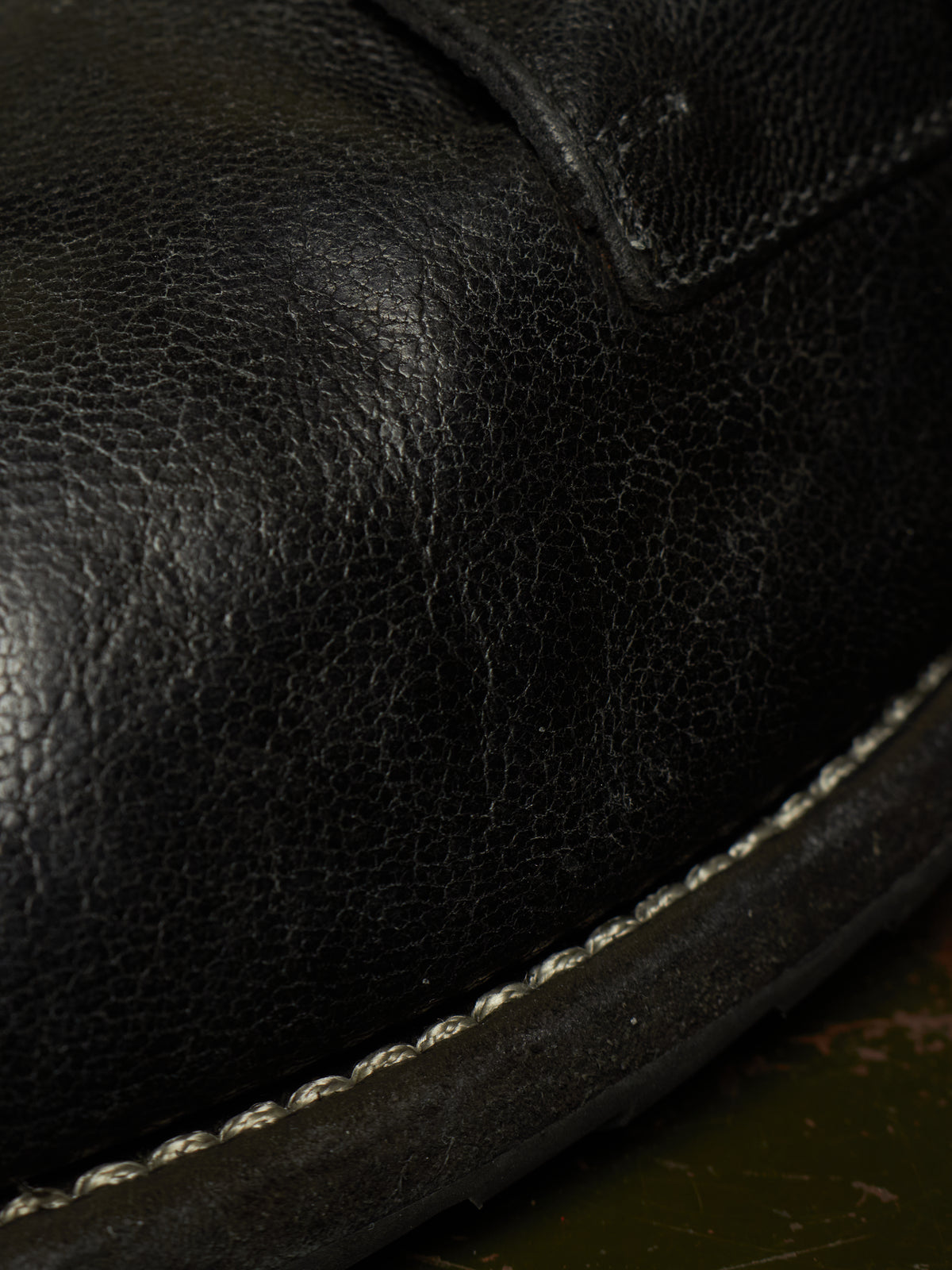 Close-up of a black leather shoe or boot showing the pebbled leather texture, stitching, and a dark sole edge.