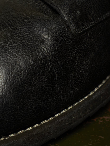 Close-up of a black leather shoe or boot showing the pebbled leather texture, stitching, and a dark sole edge.