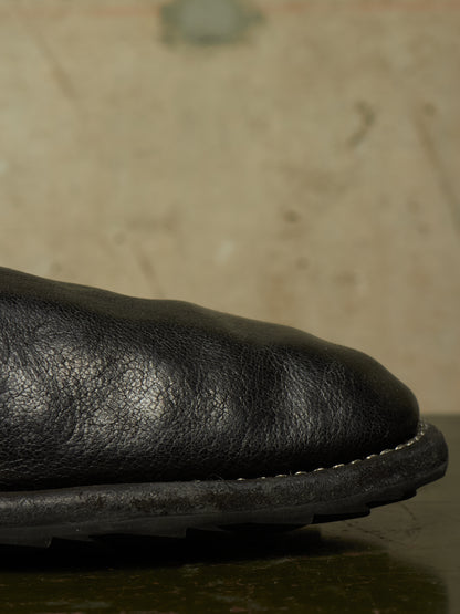 Close-up detail of a black leather boot toe showing the textured grain leather and contrast stitching against a neutral background.