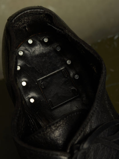 Close-up of the interior of a black leather shoe or boot, showing a black footbed with multiple small silver metal studs arranged in a circle and a rectangular black insert in the center.