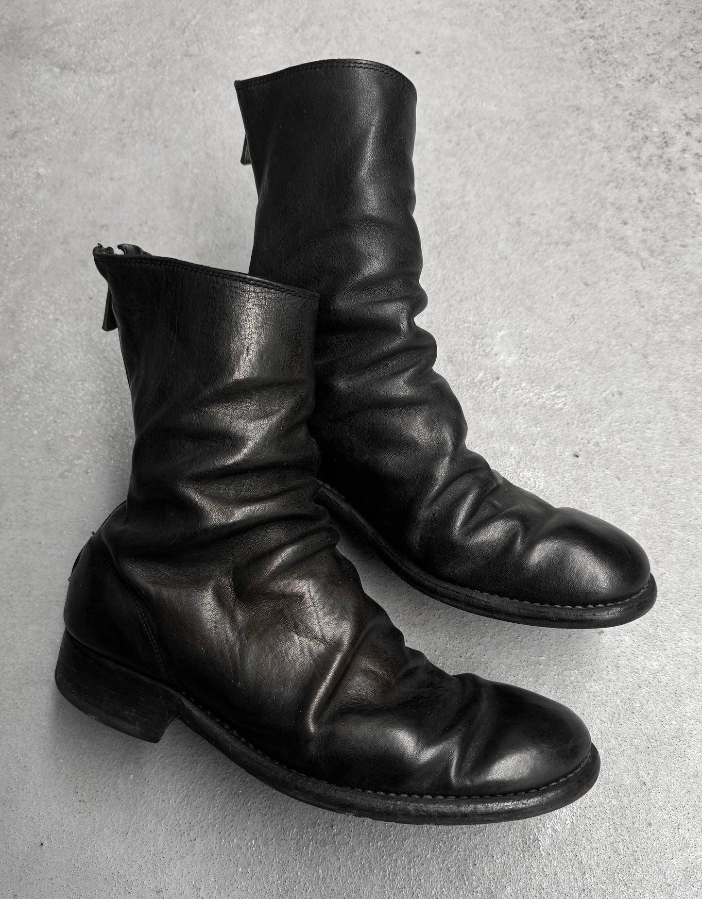 Pair of black leather boots on a gray concrete surface