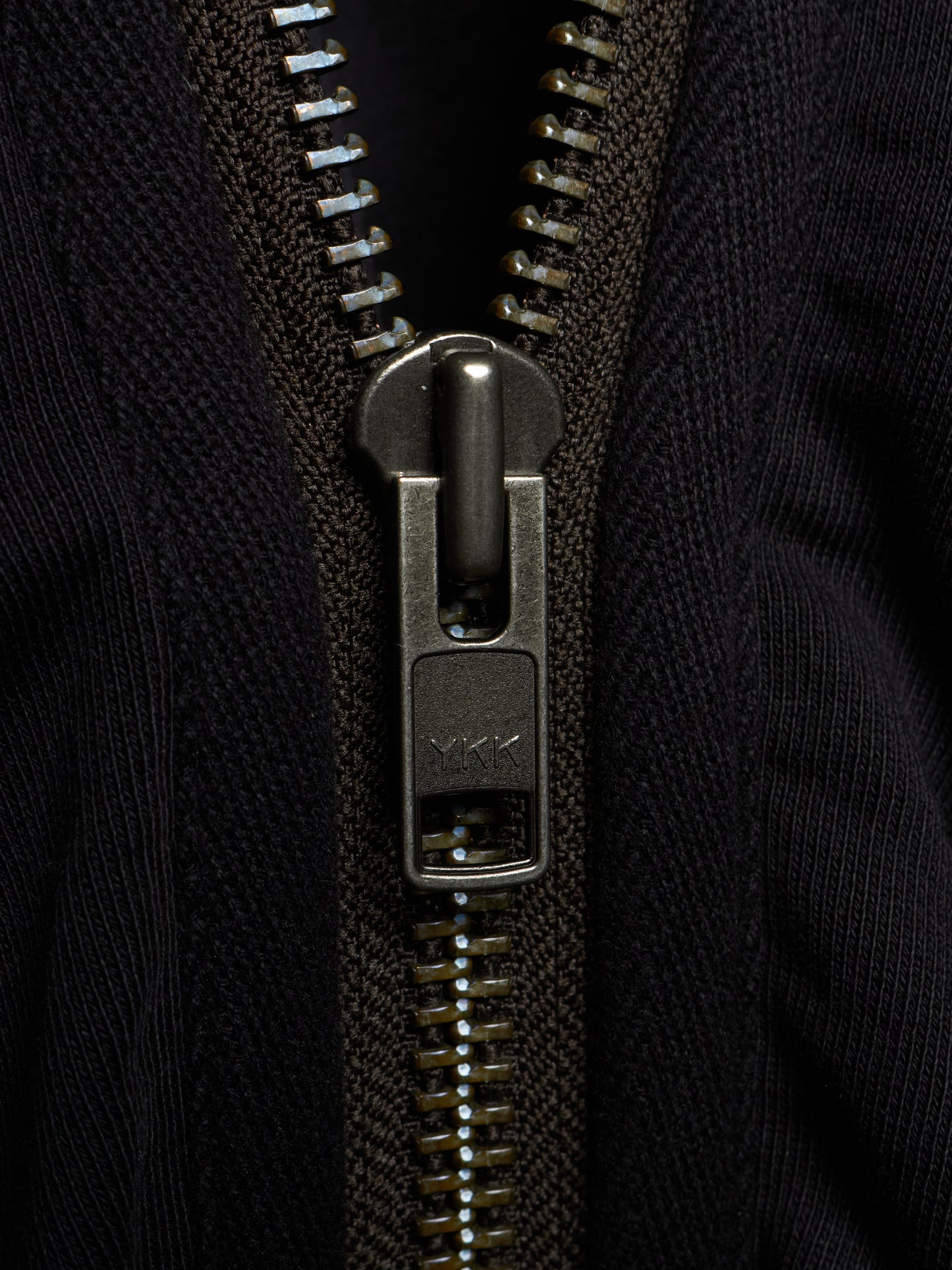 Close-up of a black ribbed knit zippered garment with a dark metallic zipper pull and teeth.