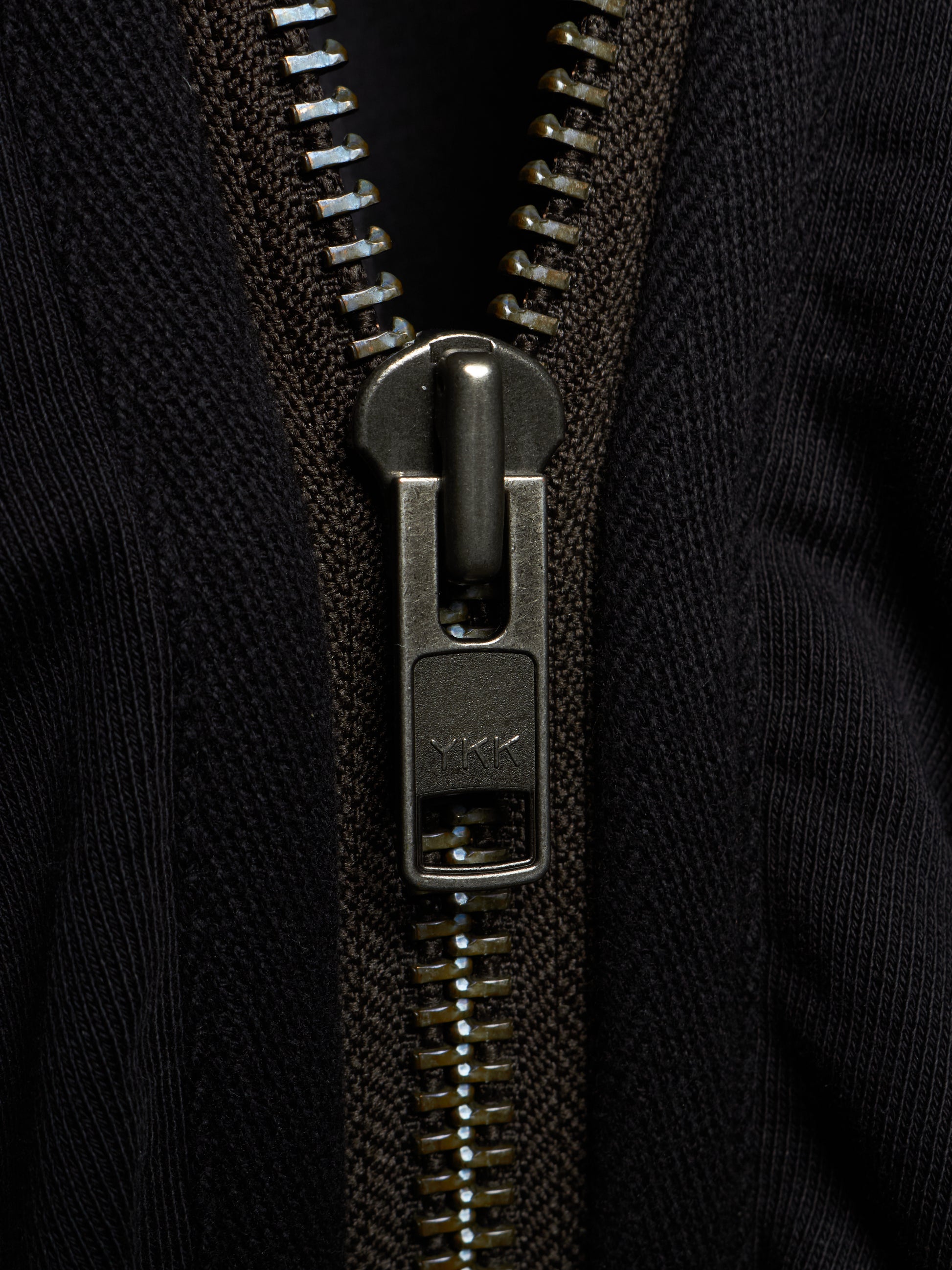Close-up of a black ribbed knit zippered garment with a dark metallic zipper pull and teeth.