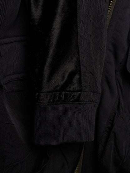 Close-up detail of a black jacket showing a ribbed fabric cuff, a satin-like black lining, and a partial gold-toned zipper.