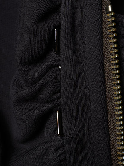 Close-up detail of a black ribbed knit garment showing a vertical seam, a metallic zipper, and small silver metal accents.