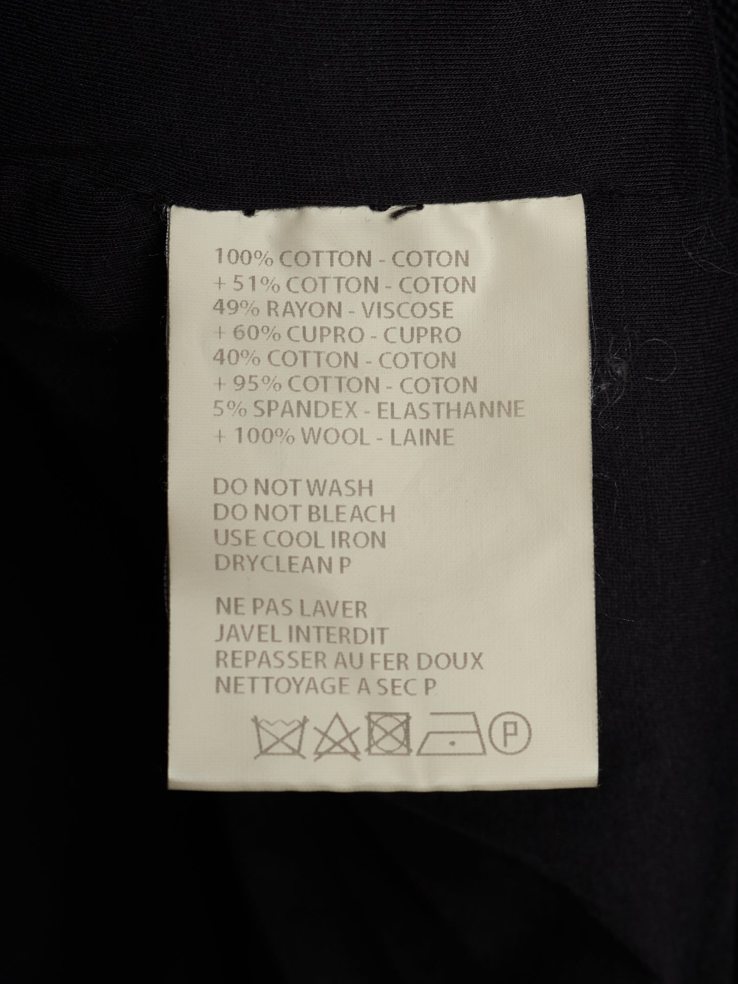 A close-up of a white garment care label sewn onto black fabric, showing text with material percentages and care instructions in English and French.