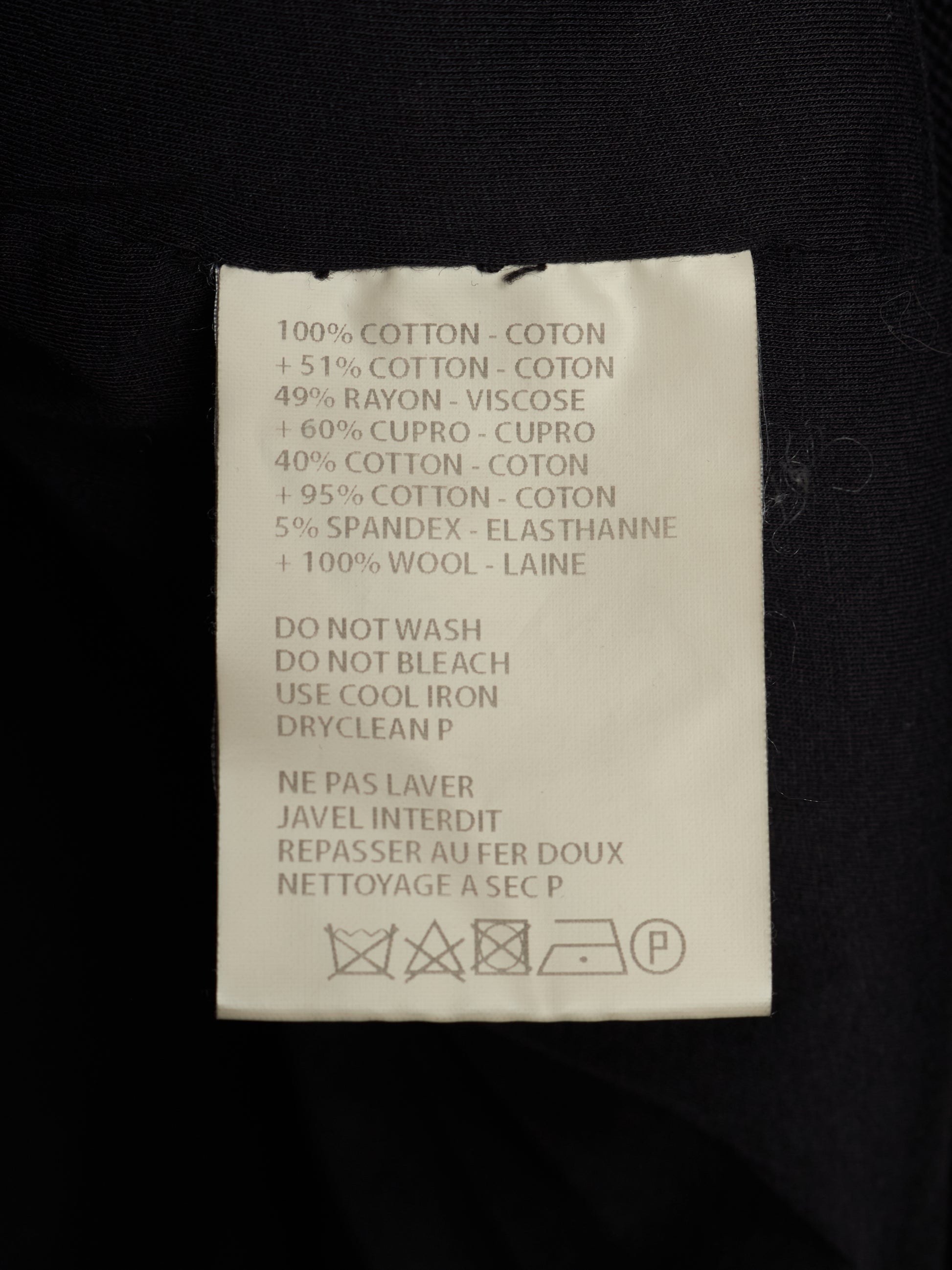 A close-up of a white garment care label sewn onto black fabric, showing text with material percentages and care instructions in English and French.