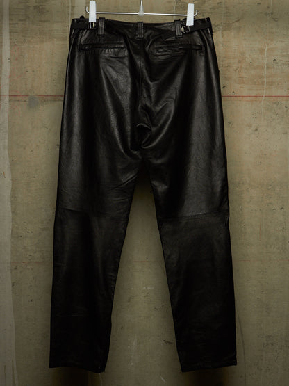 Black leather pants hanging from white clips against a textured concrete wall.