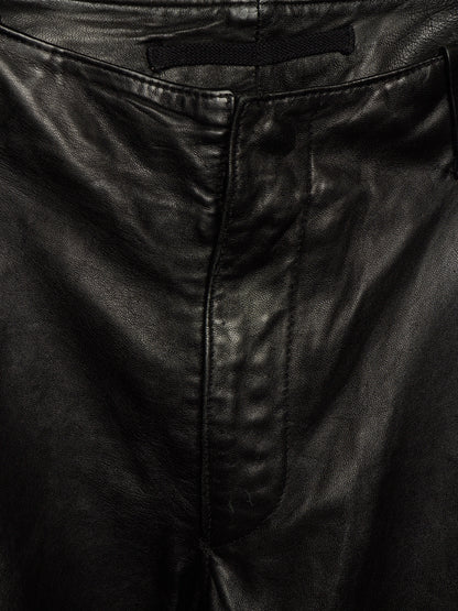 Close-up of black leather pants showing the waistband, belt loop, front seam, and texture of the material.