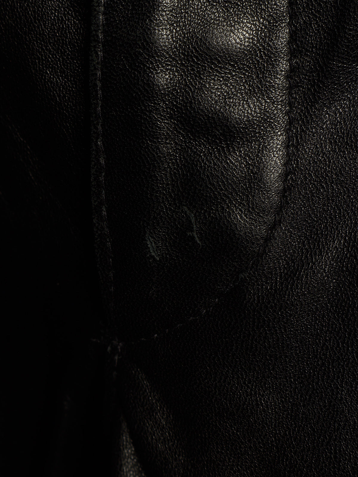 Close-up of a black leather or faux-leather material with visible grain texture and a stitched seam.