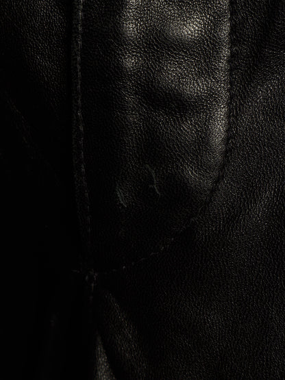 Close-up of a black leather or faux-leather material with visible grain texture and a stitched seam.