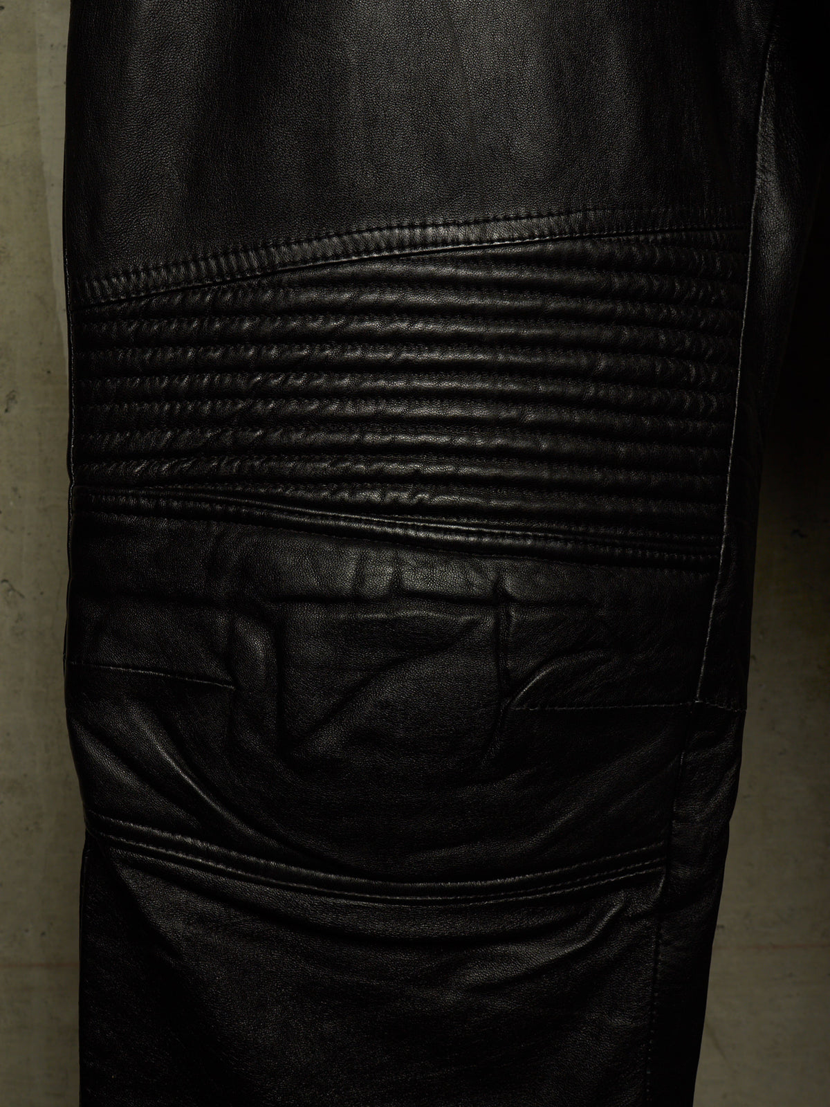 Close-up of black leather pants showing the textured biker-style leg panel with horizontal quilting and a side pocket.
