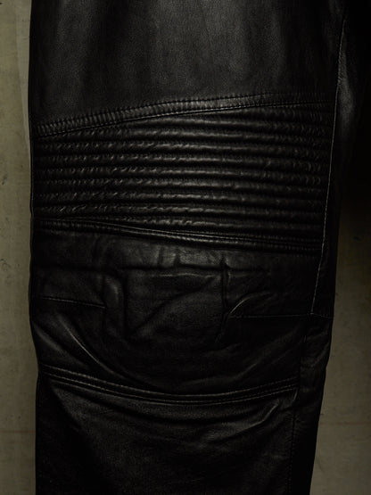 Close-up of black leather pants showing the textured biker-style leg panel with horizontal quilting and a side pocket.