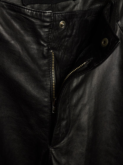 Close-up of a black leather jacket showing the front zipper, metal snap buttons, and textured leather surface.