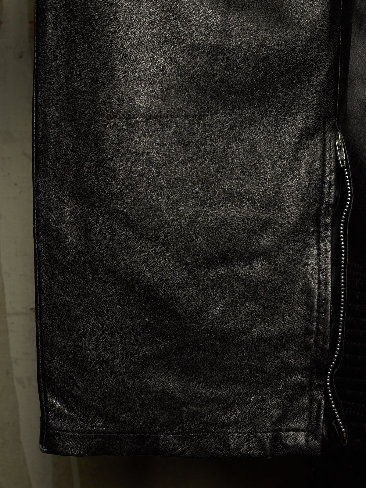 Close-up of a black leather jacket showing the texture of the leather and a silver zipper on the side.
