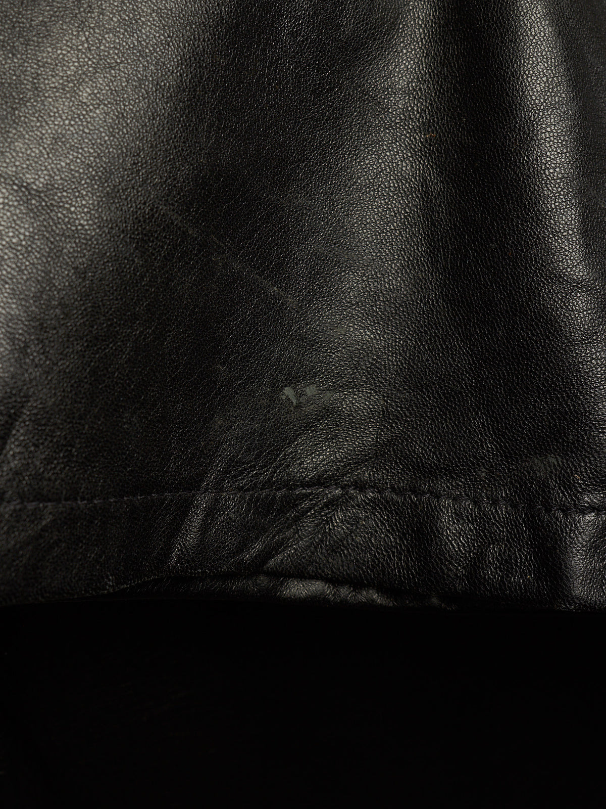 Close-up of a black leather or faux-leather surface with visible grain texture and a stitched seam near the bottom.