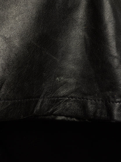Close-up of a black leather or faux-leather surface with visible grain texture and a stitched seam near the bottom.