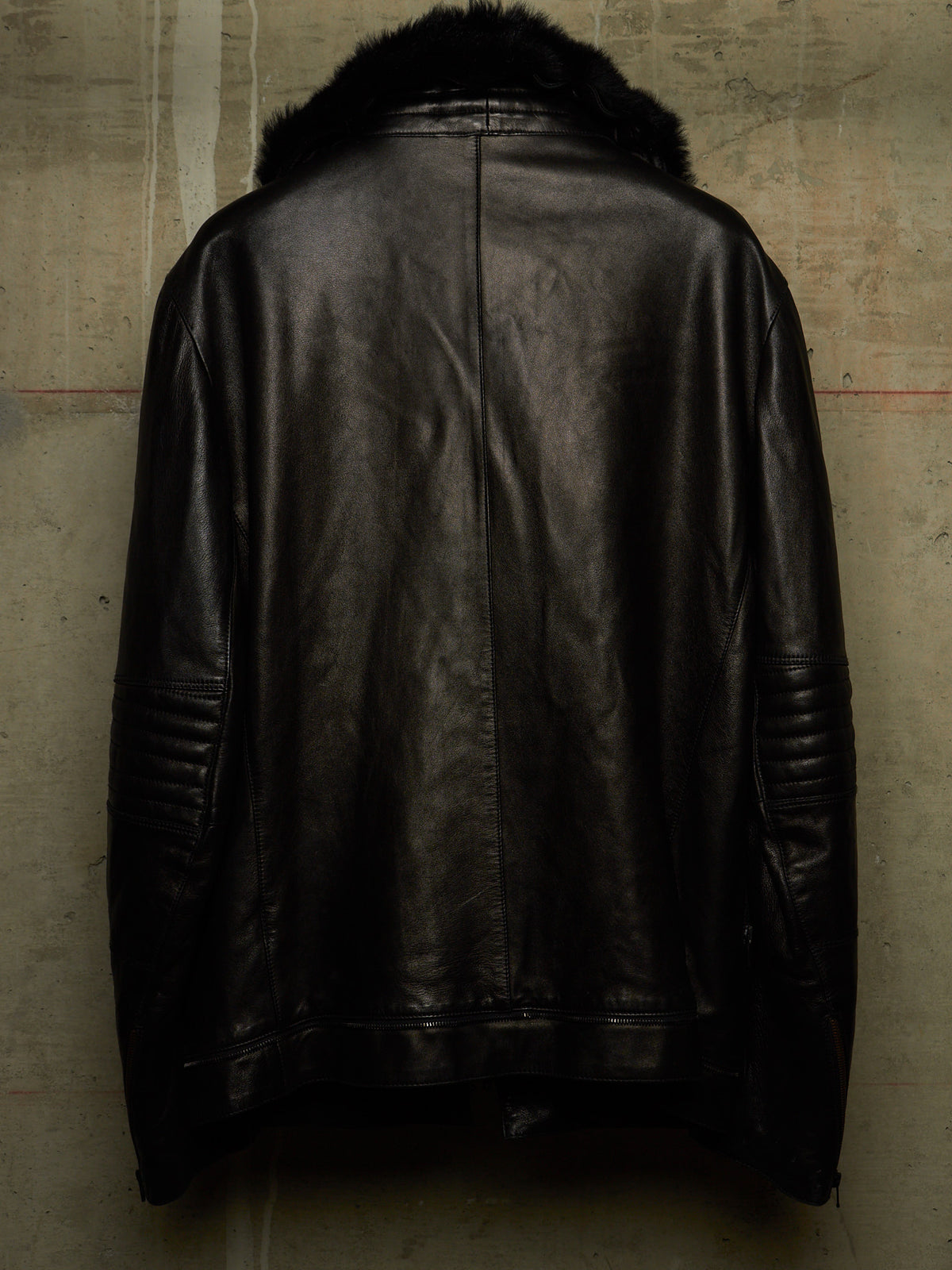 Black leather jacket with a dark fur collar, shown from the back against a textured concrete wall.