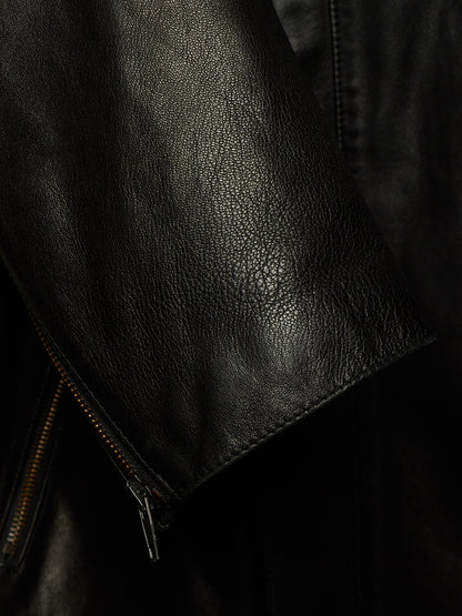 Close-up of a black leather jacket showing the pebbled texture, a zippered sleeve cuff, and dark background.