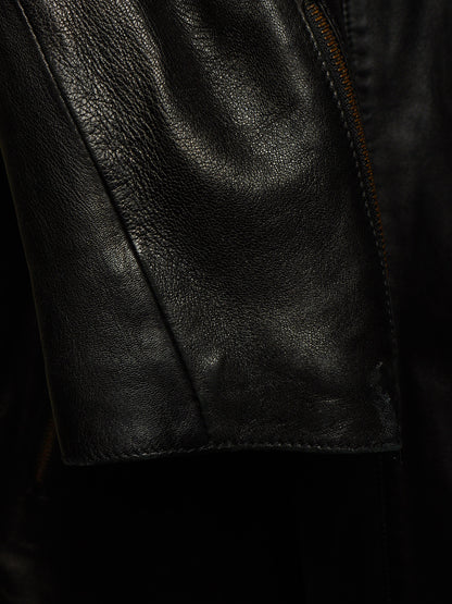 Close-up of a black leather jacket showing the textured grain, a seam, and a zipper detail.