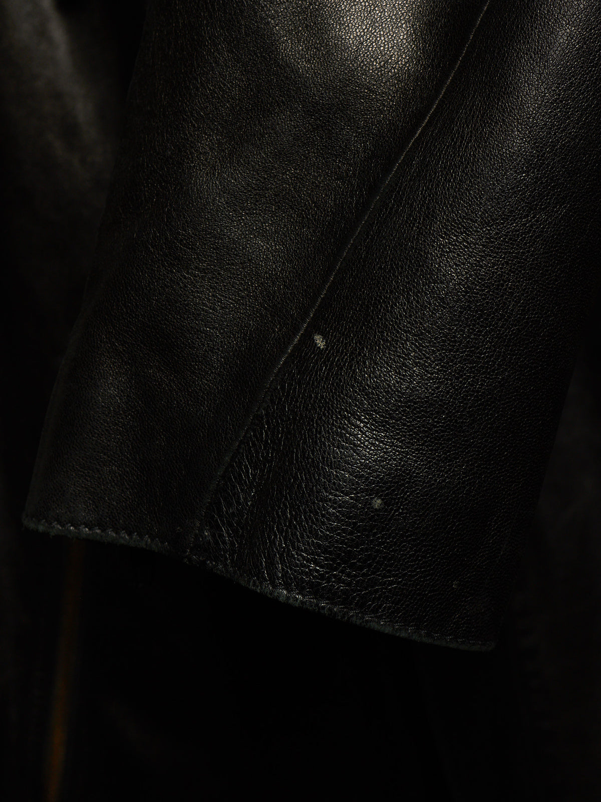 Close-up of a black leather jacket sleeve showing the pebbled texture and stitched cuff.
