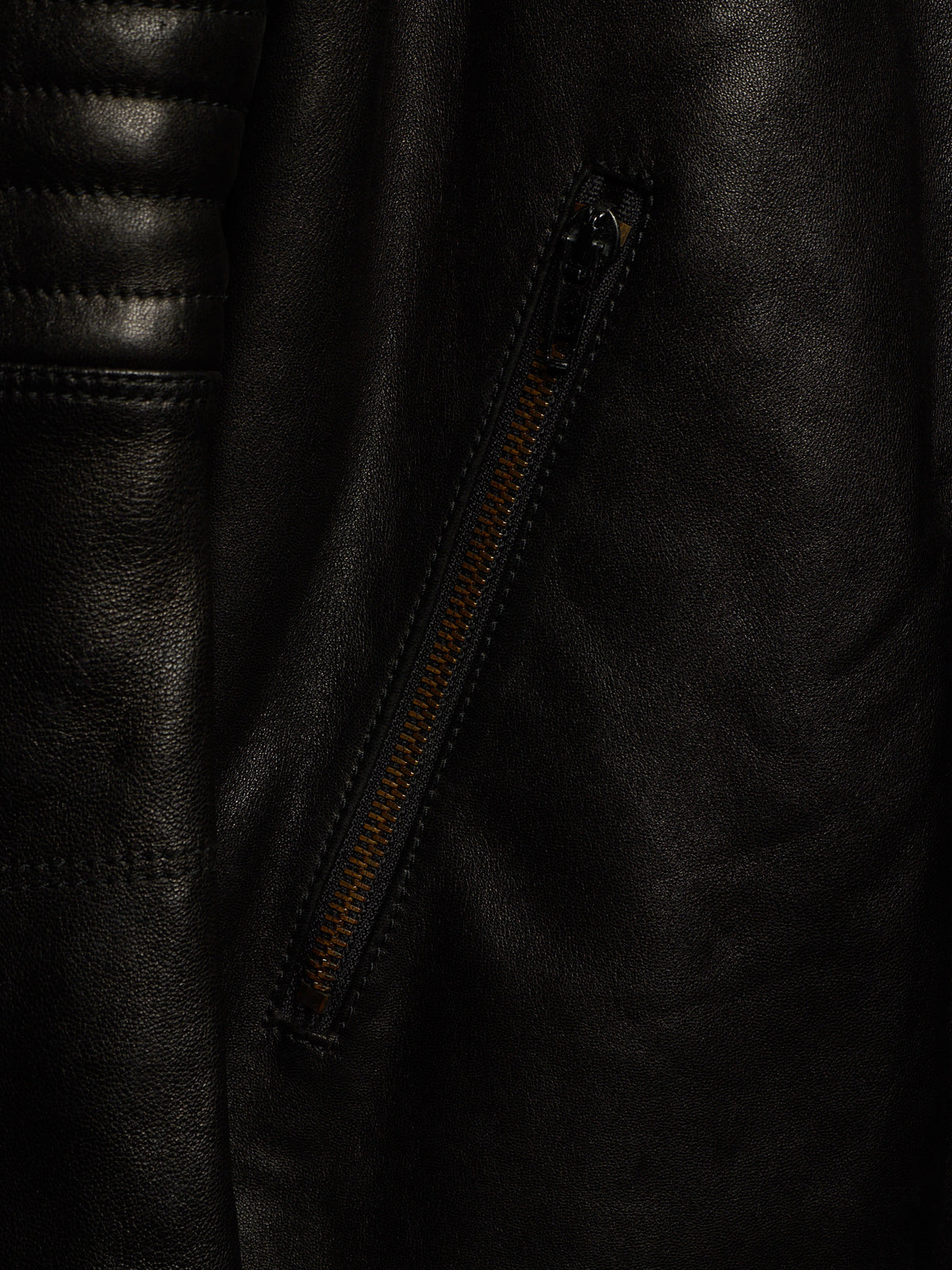 Close-up of a black leather jacket showing a diagonal zippered pocket with a contrasting orange-brown zipper pull.