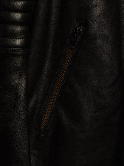 Close-up of a black leather jacket showing a diagonal zippered pocket with a contrasting orange-brown zipper pull.