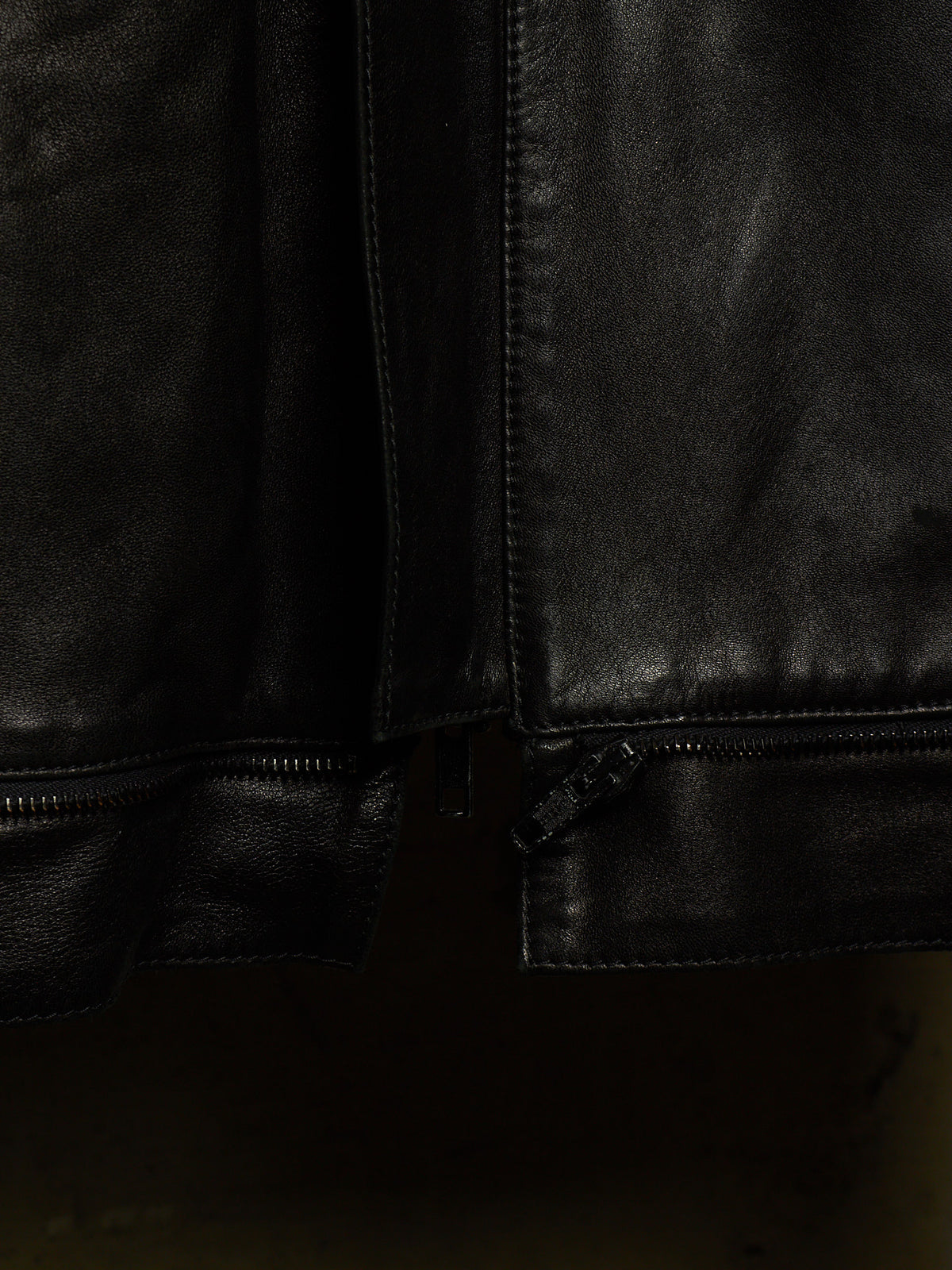 Close-up detail of a black leather jacket showing the texture, stitching, and zipper hardware.