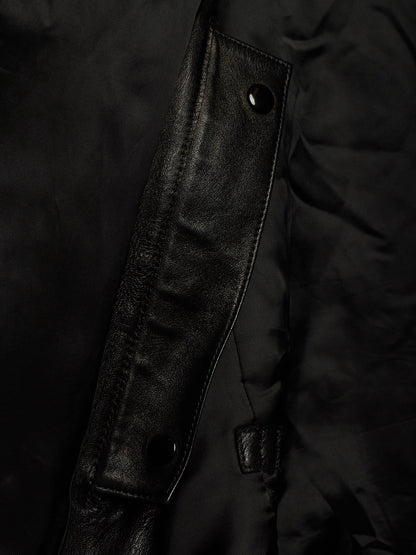 Close-up detail of a black jacket showing a smooth leather-like flap with snap buttons over a matte black fabric body.