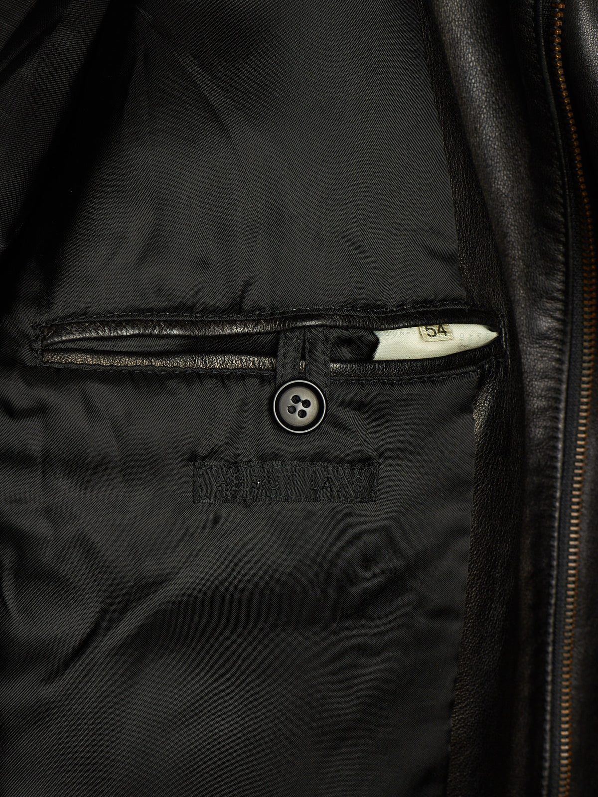 Close-up of a black leather jacket showing the interior lining, a buttoned pocket, and a zipper track.