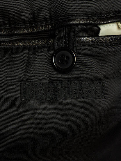 Close-up of a black quilted jacket or puffer garment showing a black button, stitched seam, and a rectangular embroidered label reading HELMET LANG.