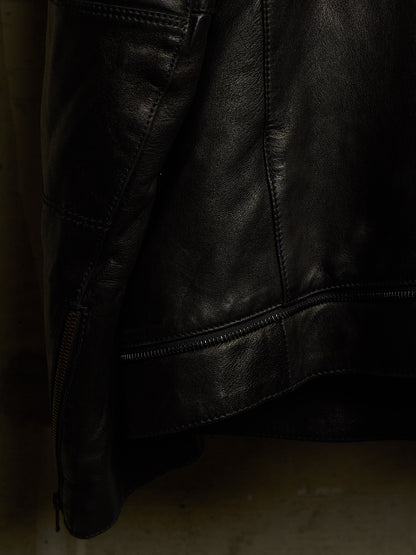 Close-up of a black leather jacket showing the texture, stitching, and a zipper detail against a dark background.