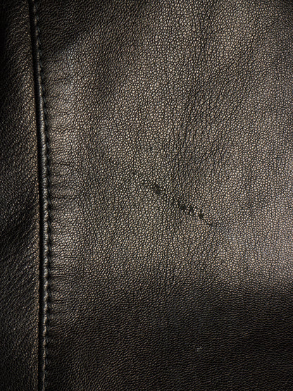 Close-up of black leather texture with visible grain, stitching along the left edge, and a small scratch-like mark across the center.