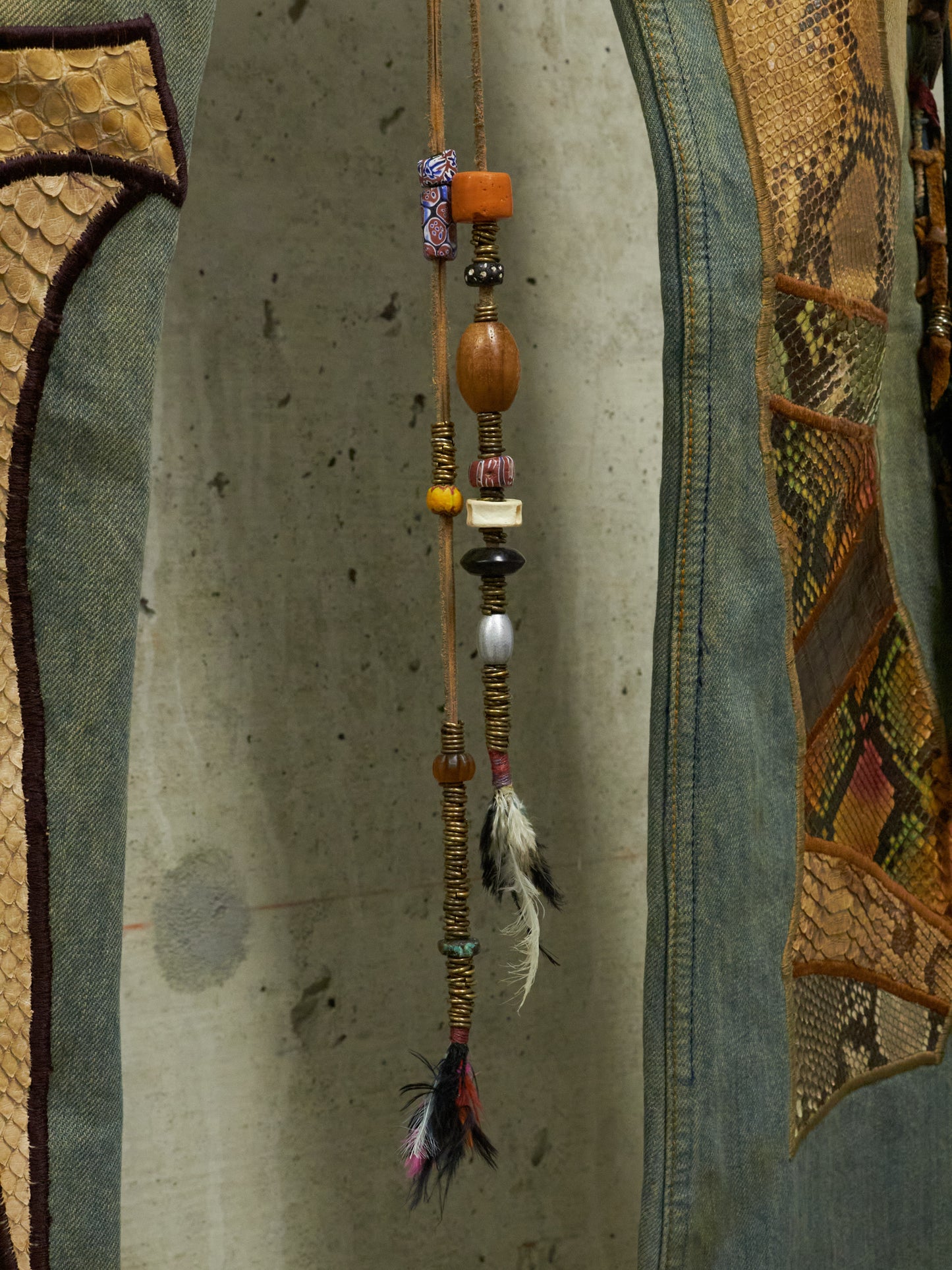 Decorative hanging with beads and feathers against a textured wall.