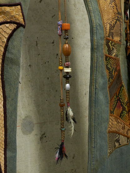 Decorative hanging with beads and feathers against a textured wall.