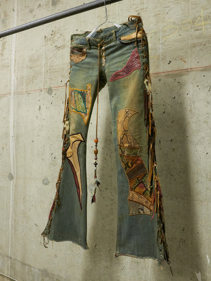 Decorative jeans with patches and fringe hanging against a concrete wall.