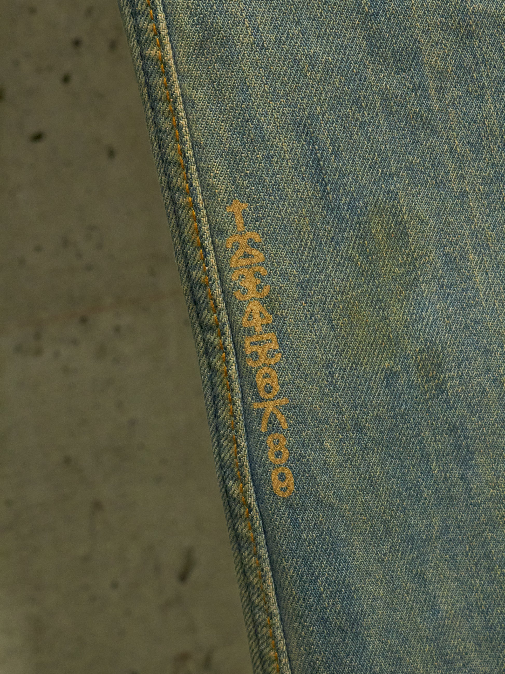 Close-up of blue denim fabric with yellow stitching on a textured gray background